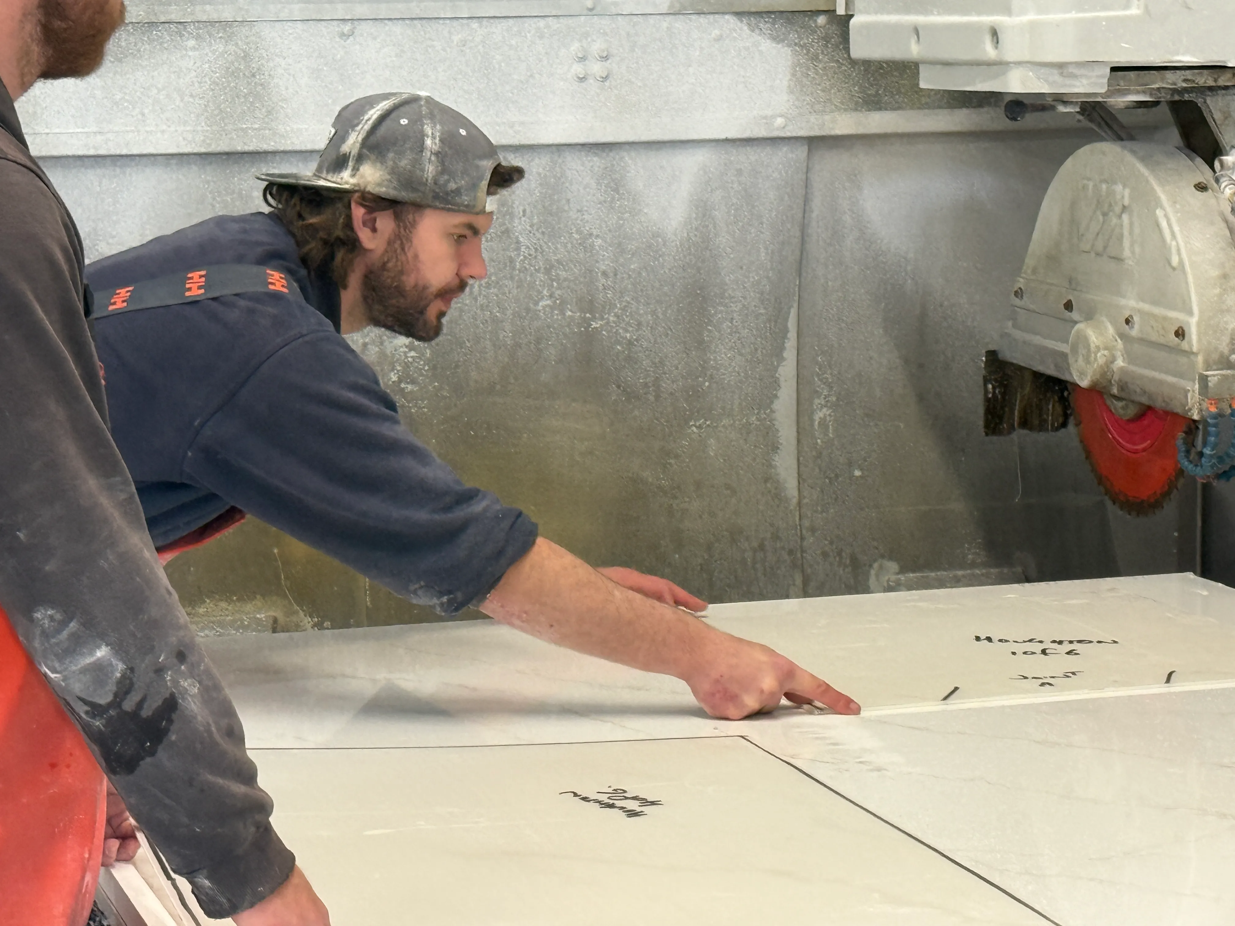 Team positioning a marked-up stone slab on the CNC bridge saw