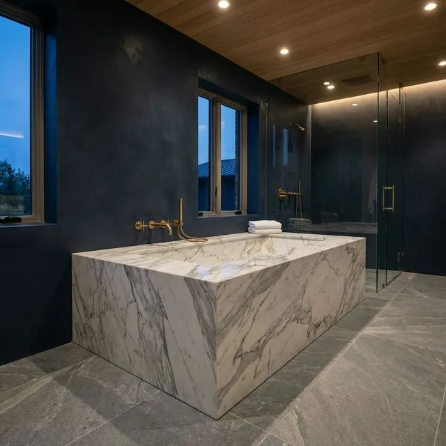 Luxury modern bathroom featuring a bespoke rectangular stone bath clad in calacatta marble slab panels with brushed brass fixtures