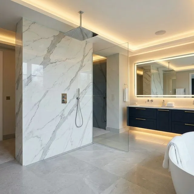 Luxury walk-in shower with full-height calacatta marble-effect stone wall panels and frameless glass screen